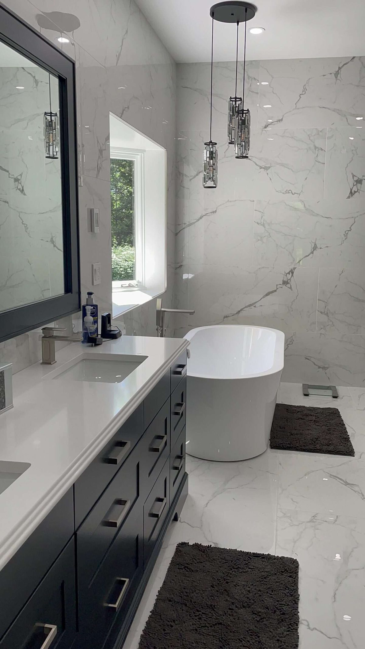 Bathroom with marble-look tile on the walls and floor, a navy double vanity and a freestanding tub