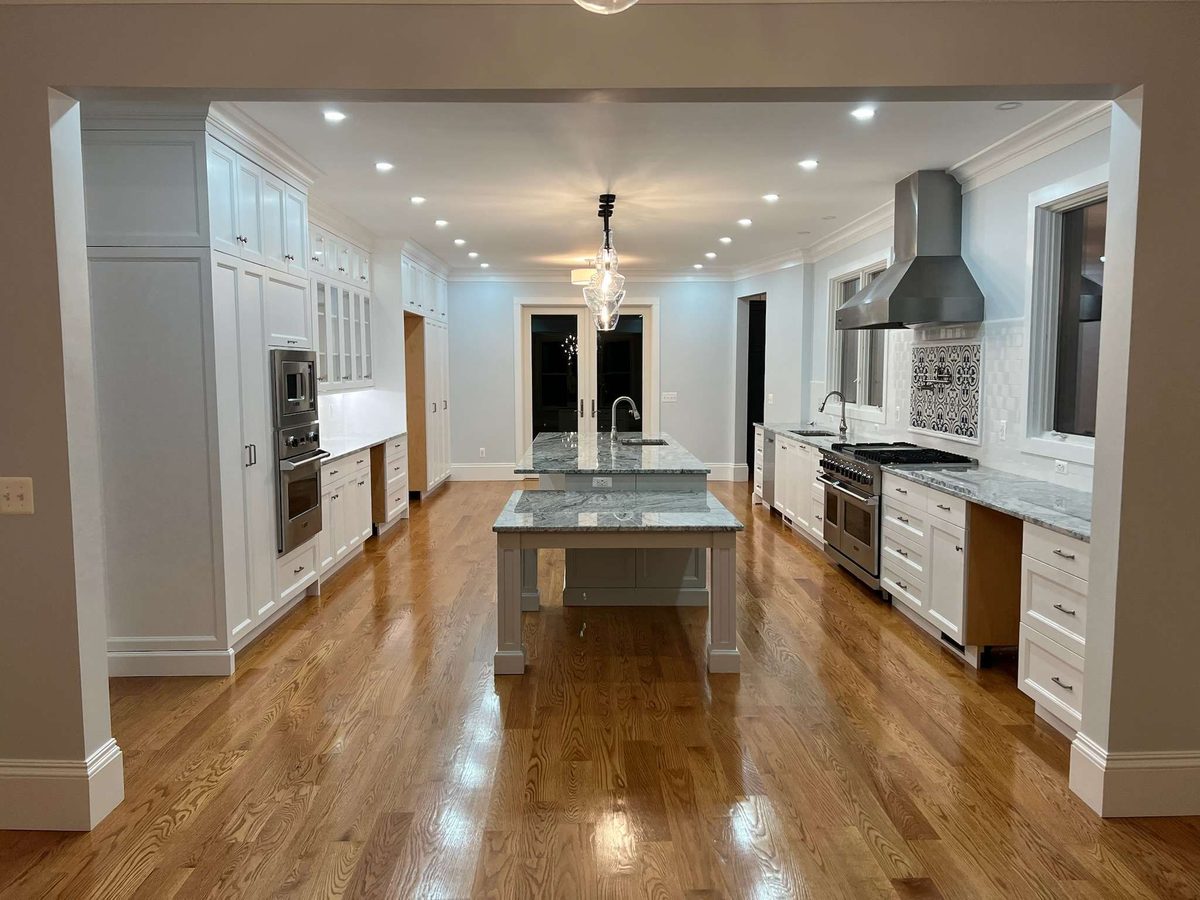 White kitchen with a long stone-topped island, a stainless range hood and glossy hardwood floors