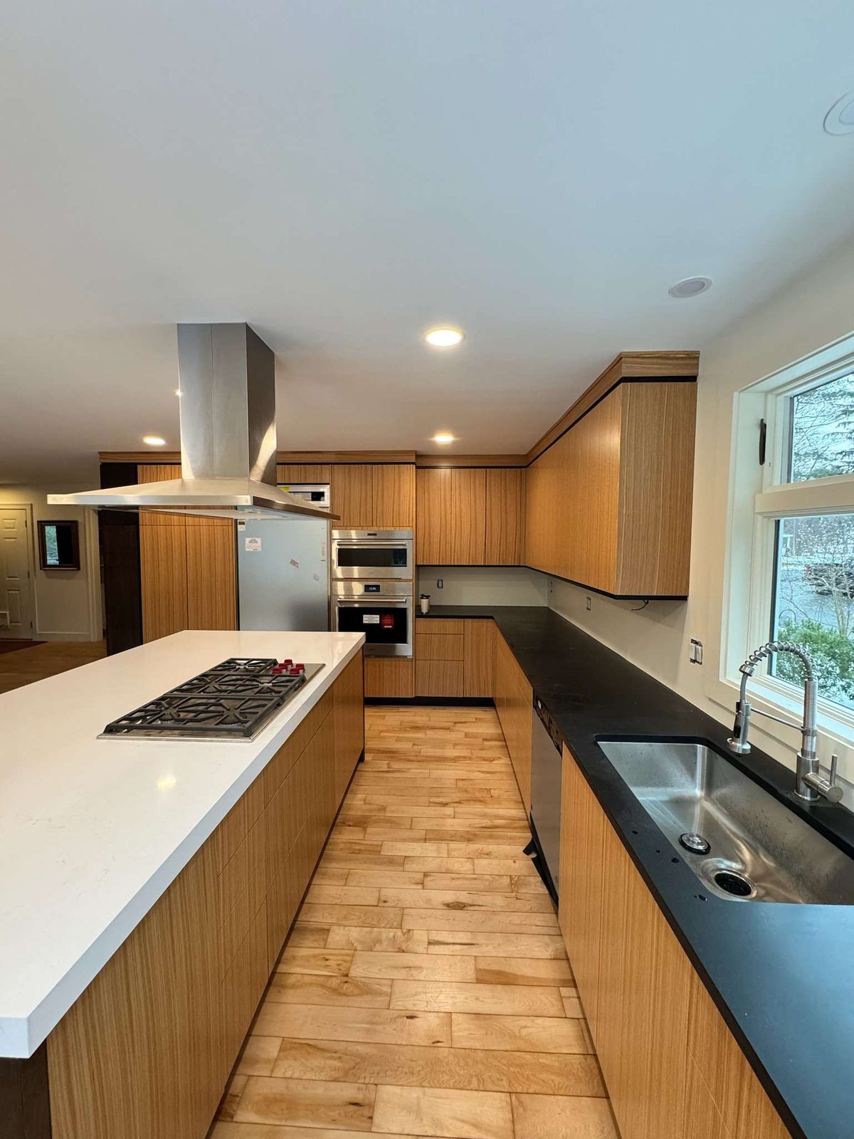 Long island with a gas cooktop facing wood-grain cabinetry and a black countertop along the windows