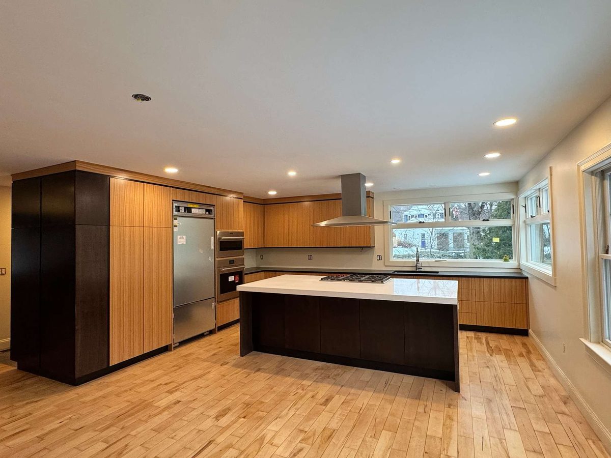 Open kitchen with tall dark cabinets, built-in stainless refrigerator and wall ovens, and a large window wall