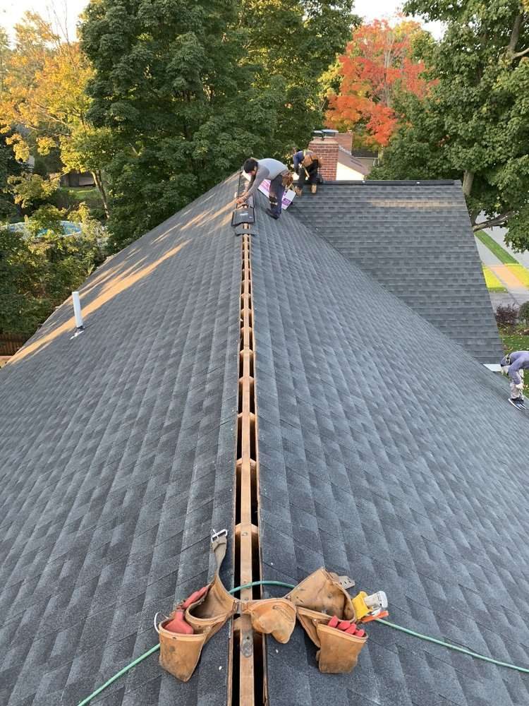 Roofers working along the ridge of a new asphalt shingle roof, with tool belts on the ridge